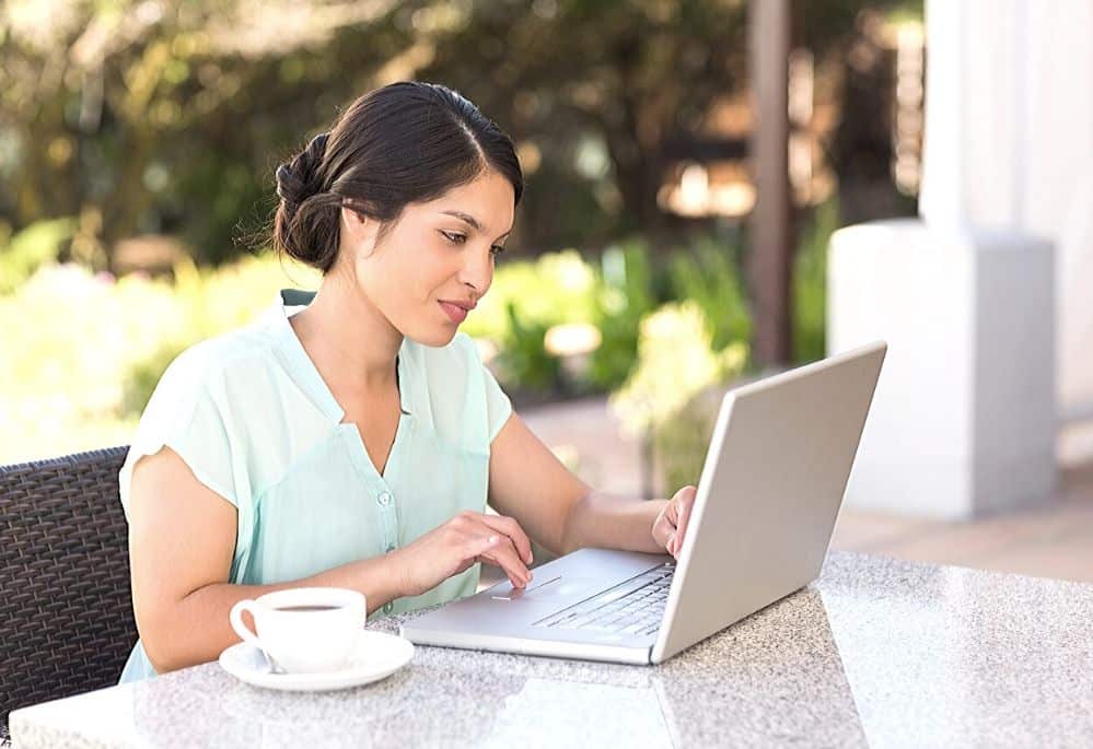 Woman at table drinking coffee and working from home on laptop
