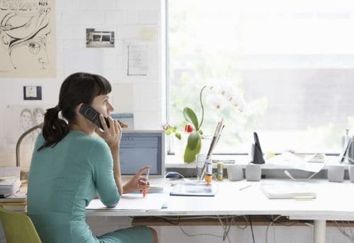 Female Virtual Assistant Sitting at Desk on phone in front of a pc providing a virtual assistant service