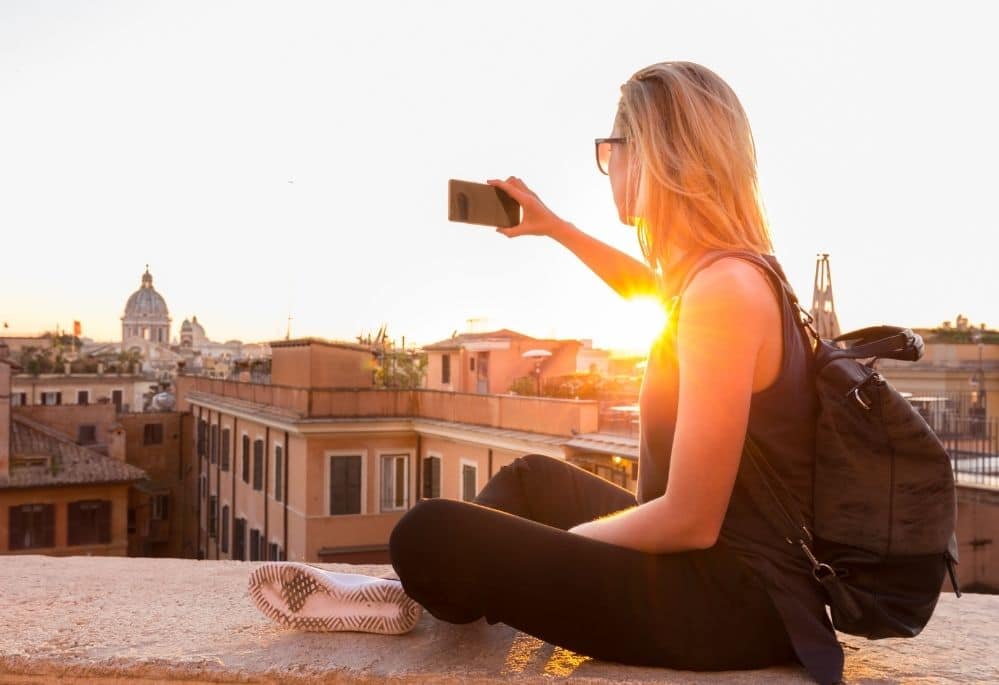 Woman taking picture of sunset cityscape on smartphone using one of best apps to sell photos