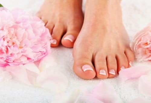 Bare feet of woman walking on pink carnation flowers and petals