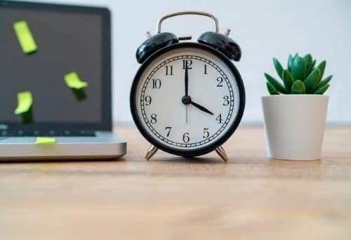 image of laptop, succulent plant and a black alram clock with hands pointing to four o clock showing end time for a work day.