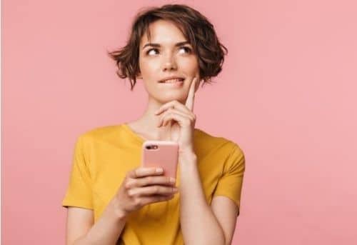 woman with short brown hair in yellow t-shirt thinking about where she can sell her feet photos that are on her pink smartphone.